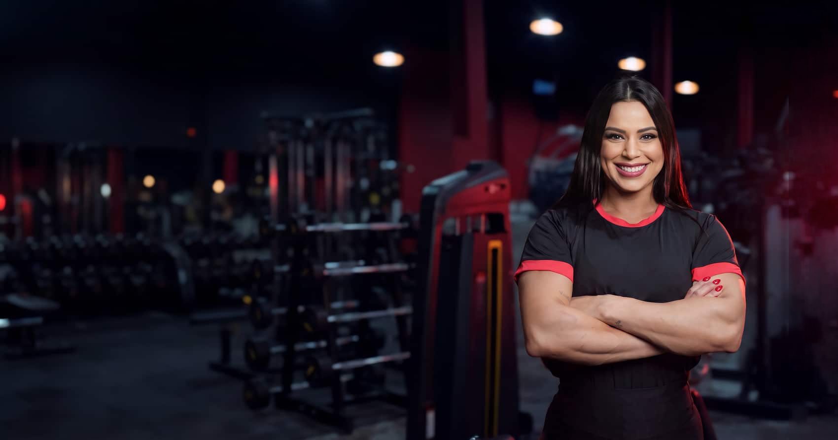Jéssica Felipe sorrindo, de braços cruzados, em uma academia de luz baixa